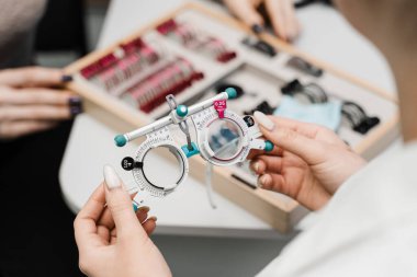 Optalmolojistin ellerinde yakın çekim deneme çerçevesi gözlüğü. Kısa ya da uzun görüşlü bir kızın göz görme sistemini incelemek için deneme gözlüğü seçimi için göz doktoruyla muayene