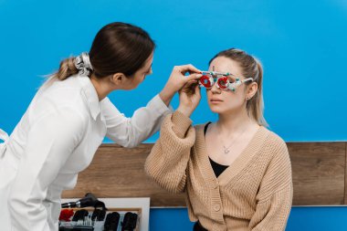 Oftalmolog, kızın üzerinde deneme çerçevesi gözlüğü takıyor. Kısa ya da uzun görüşlü bir kızın göz görme sistemini incelemek için deneme gözlüğü seçimi için göz doktoruyla muayene
