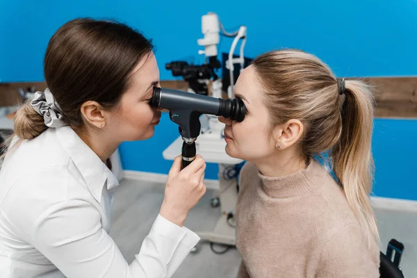 Optometrist göz doktoruna optalmoskop kullanarak bakar. Oftalmoskopi. Oftalmolog, göz doktoru olan bir kadının gözlerini inceliyor. Klinikteki bir optometriste danışmanlık
