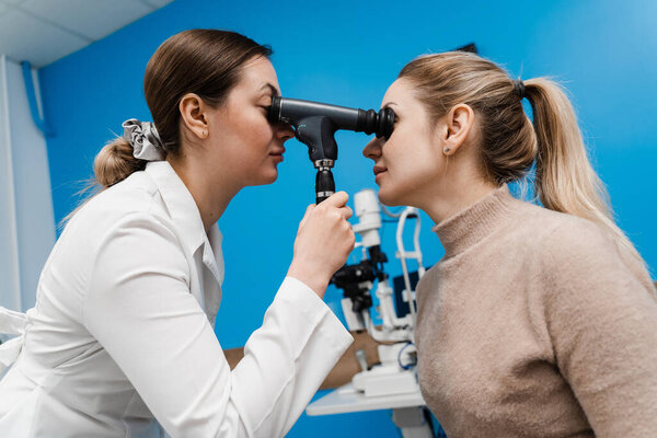 Optometrist looks into eye using an ophthalmoscope. Ophthalmoscopy. Ophthalmologist examines the eyes of woman with ophthalmoscope. Consultation with an optometrist in a medical clinic