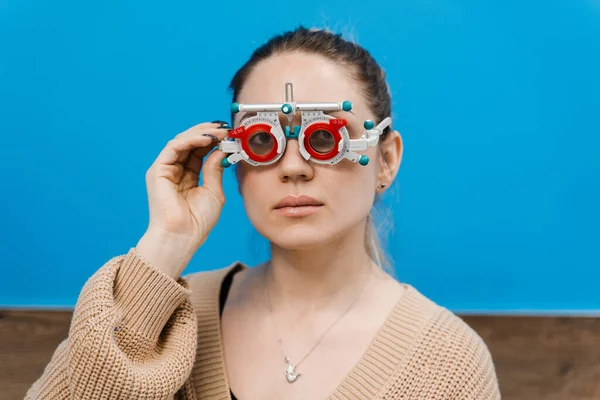 Girl in trial frame glasses on blue background. Examination with ophthalmologist for selection of trial glasses frame to examine eye visual system of girl with short or long power vision