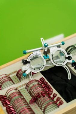 Yakın plan deneme çerçevesi gözlükleri ve yeşil arka planda lens seti. Kısa veya uzun görüşlü hastaların göz görme sistemini incelemek için oftalmoloji ekipmanları