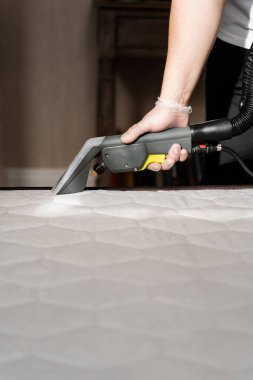 Temizlikçi kuru temizleme makinesiyle yataktan toprak çıkarıyor. Evde kuru temizleme için sökücü kullanan döşek temizleniyor