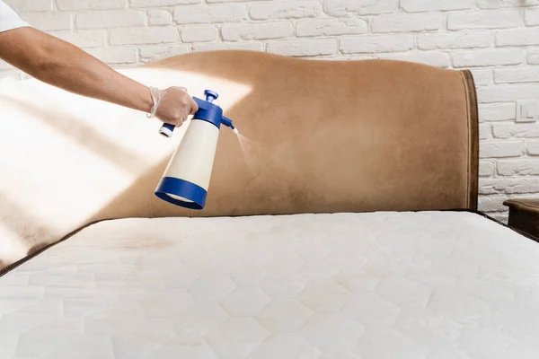 Mattress cleaning. Spraying detergent on mattress for dry cleaning. Professional cleaner in gloves is pouring detergent on mattress for removing stains and dirt