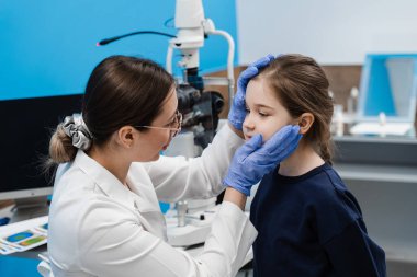 Pediatrik göz doktoru, çocuğun gözlerini ve göz bebeğini inceliyor. Göz iltihabı tedavisi ve görme düzeltmesi için göz hastalıkları kliniğinde çocuklara danışmanlık
