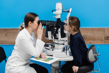 Kesik lambasıyla pediatrik göz doktoru çocuğun gözlerini ve korneasını inceliyor. Göz doktoru, gözleri ve korneayı teşhis etmek için kesik lambadan gelen ışıkla çocuğun gözünü aydınlatıyor.