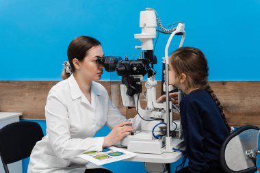 Göz doktoru, gözleri ve korneayı teşhis etmek için kesik lambadan gelen ışıkla çocuğun gözünü aydınlatıyor. Kesik lambasıyla pediatrik göz doktoru çocuğun gözlerini ve korneasını inceliyor.