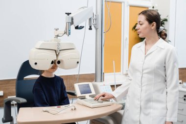 Çocuk pediatrik göz doktorunun muayenesi sırasında phoropter 'e bakar. Kırılma hatasını ölçmek ve gözlük reçetesi için bilgi belirlemek için Phoropter