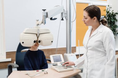 Kırılma hatasını ölçmek ve gözlük reçetesi için bilgi belirlemek için phoropter. Çocuk, pediatrik göz doktorunun göz muayenesi sırasında phoropter 'e bakar.