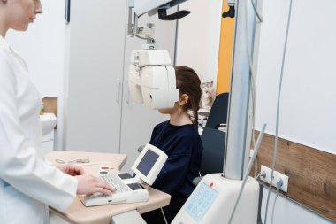 Kırılma hatasını ölçmek ve gözlük reçetesi için bilgi belirlemek için phoropter. Çocuk, pediatrik göz doktorunun göz muayenesi sırasında phoropter 'e bakar.