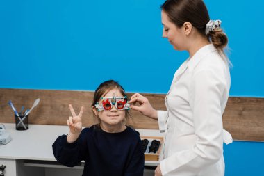 Çocuğun göz görme sistemini incelemek için deneme gözlüğü çerçevesi seçimi için pediatrik göz doktoruyla çocuk muayenesi. Oftalmolog, gözlüklerin deneme çerçevesi için lensleri seçti