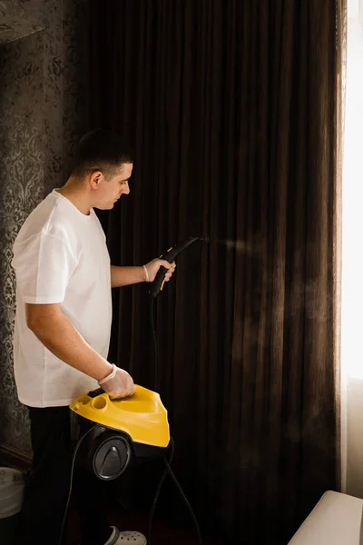Curtains steam cleaning process. Disinfection and dry cleaning of curtain at home. Cleaner is steaming the curtains using a professional steam machine