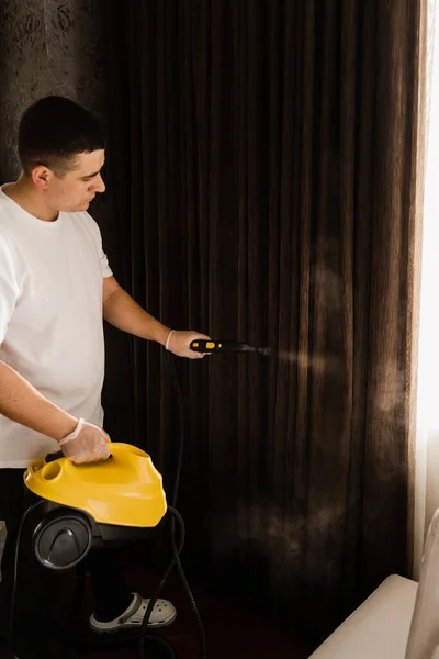 クリーナーは プロの蒸気機械を使用してカーテンを蒸しています 蒸気洗浄プロセスをカバーしています 消毒と自宅でカーテンの乾燥洗浄 — ストック写真