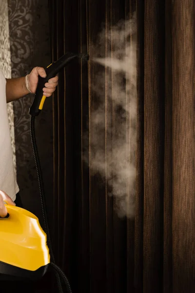 Disinfection and dry cleaning of curtain at home. Cleaner is steaming the curtains using a professional steam machine. Curtains steam cleaning process