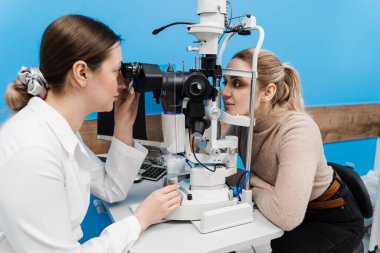 Kesik lambalı bir oftalmolog kadının gözlerini ve korneasını inceliyor. Göz doktoru, göz ve kornea teşhisi koymak için kesik lambadan gelen ışıkla hastanın gözünü aydınlatıyor.