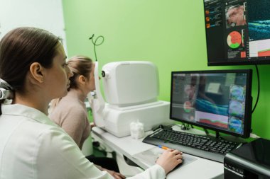 Optik tutarlılık tomografisi kullanan hastaların gözleri inceleniyor. Göz arkası görüntülerini oluşturmak için optik eşkenar tomografi tomografisi. Oftalmolog kadın hastaların kornealarını tarıyor.
