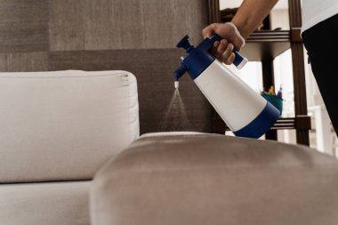 Spraying detergent on couch for dry cleaning using extractor machine. Process of dry cleaning for removing stains and dirt from couch at home. Professional cleaning service