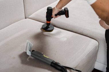 Kuru temizleme için fırçalı matkapla kanepede deterjan sürüyorsun. Kuru temizleme için evdeki kanepeye deterjan sürüyorum.