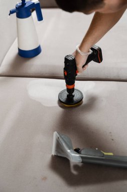 Kuru temizleme için fırçalı matkapla kanepede deterjan sürüyorsun. Kuru temizleme için evdeki kanepeye deterjan sürüyorum.