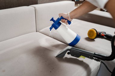 Process of dry cleaning for removing stains and dirt from couch at home. Professional cleaning service. Spraying detergent on couch for dry cleaning using extractor machine