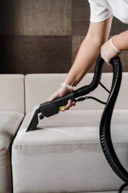 Temizlikçi kuru temizleme makinesiyle döşenmiş koltuktan toprak çıkarıyor. Temizlikçi, kuru temizleme mobilyaları için elektrikli süpürge sökücü ile kanepeyi temizliyor.