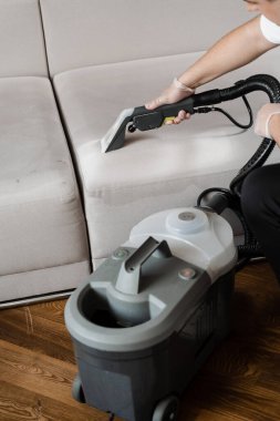 Kuru temizlemeden sonra elektrikli süpürge sökücü makinesiyle kanepede kuyruk. Ev temizlik hizmeti temizleyicisi kuru temizleme makinesiyle kanepenin tozunu ve pisliğini temizliyor.
