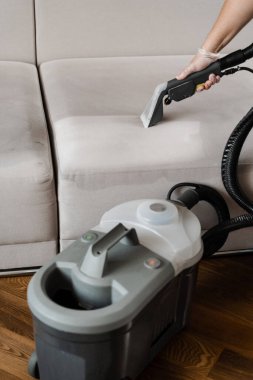 Kuru temizlemeden sonra elektrikli süpürge sökücü makinesiyle kanepede kuyruk. Ev temizlik hizmeti temizleyicisi kuru temizleme makinesiyle kanepenin tozunu ve pisliğini temizliyor.