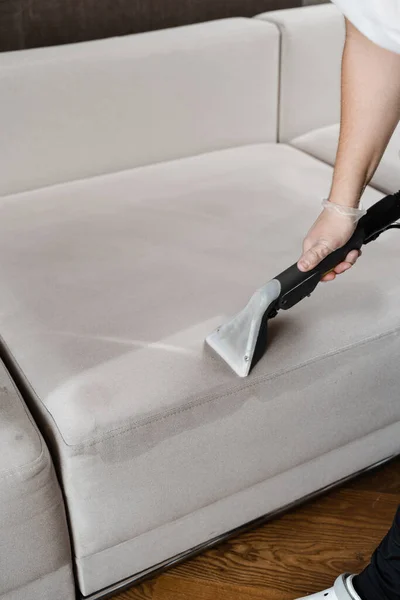 Housekeeper is extracting dirt from upholstered sofa using dry cleaning extraction machine. Cleaner is cleaning couch with washing vacuum cleaner extractor machine for dry clean upholstered furniture