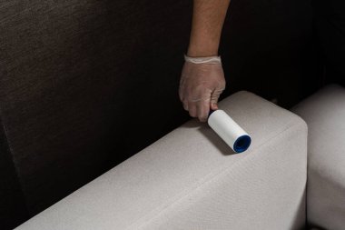 Kedi ve köpek kılından pamuk rulo kullanarak kanepeyi temizliyorum. Temizlikçi, yakın çekim temizleyicisiyle kanepeden ipliği kaldırıyor.