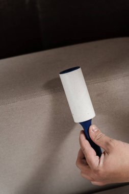 Kedi ve köpek kılından pamuk rulo kullanarak kanepeyi temizliyorum. Temizlikçi, yakın çekim temizleyicisiyle kanepeden ipliği kaldırıyor.