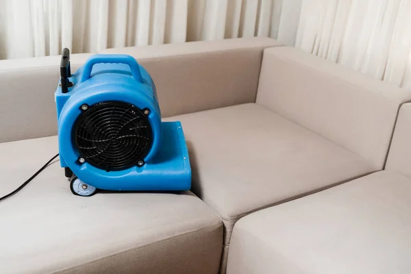 Floor dryer blower fan machine drying wet couch after dry cleaning of upholstered furniture. Process of drying sofa using floor dryer blower fan machine