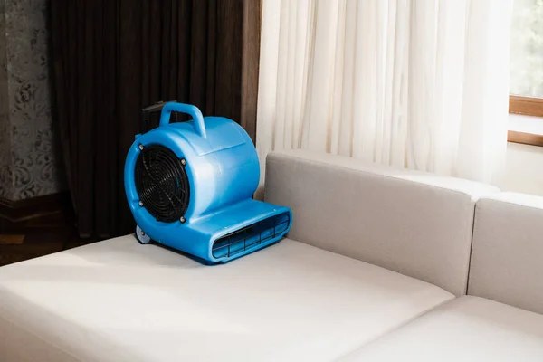 Process of drying sofa using floor dryer blower fan machine. Floor dryer blower fan machine drying wet couch after dry cleaning of upholstered furniture