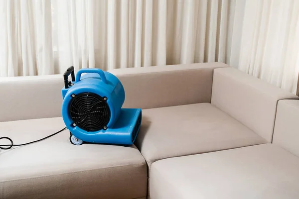 Floor dryer blower fan machine drying wet couch after dry cleaning of upholstered furniture. Process of drying sofa using floor dryer blower fan machine