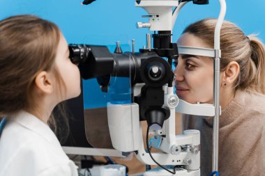 Doktor çocuk doktoru, doktor önlüğündeki kesik lambayla. Çocuk kesik lambadan bakıyor ve hastanın gözlerini ve korneasını inceliyor. Optalmolojinin yaratıcı kavramı