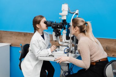 Doktor çocuk doktoru, doktor önlüğündeki kesik lambayla. Çocuk kesik lambadan bakıyor ve hastanın gözlerini ve korneasını inceliyor. Optalmolojinin yaratıcı kavramı