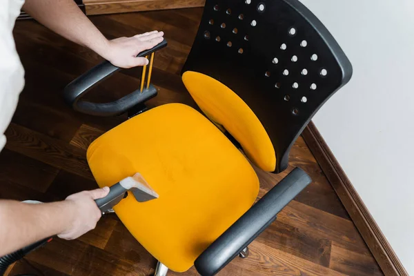 Cleaner is cleaning chair with washing vacuum cleaner extractor machine for dry clean top view. Housekeeper is extracting dirt from yellow armchair using dry cleaning extraction machine