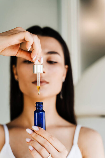 Girl is holding pipette with hyaluronic serum or acid in hands. Young woman with acid dropper in hands