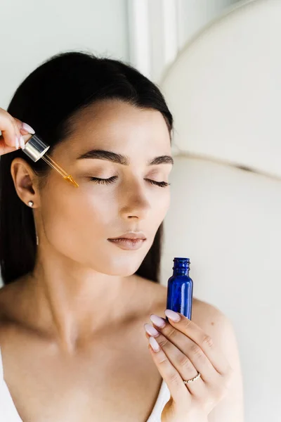 stock image Young woman with acid dropper is applying drops of acid on her skin. Girl applying hyaluronic serum with pipette on face