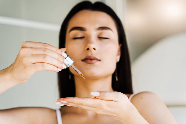 Девушка с гиалуроновой кислотой или сывороткой пипетки в руках крупным планом. Молодая женщина наносит увлажняющую сыворотку на кожу
