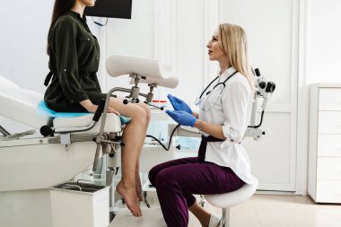 Gynecologist does colposcopy procedure to closely examine cervix, vagina and vulva of girl in gynecology clinic. Gynecologist is looking in colposcope for detail examination of disease clipart