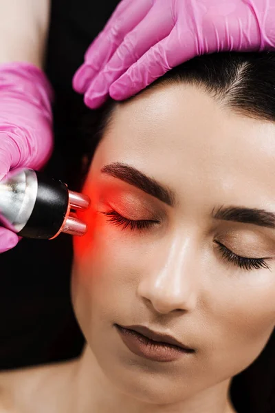 Radio frequency lifting with red light for young woman close-up. Dermatologist is doing radio frequency RF skin tightening. RF facelift firms and lifts sagging skin