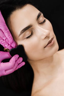 Taş kazıyıcı kullanarak kız yüzü için Gouache masajı. Güzellik uzmanı Gua Sha masajı yapar kan dolaşımını ve yüz rengini iyileştirmek için.