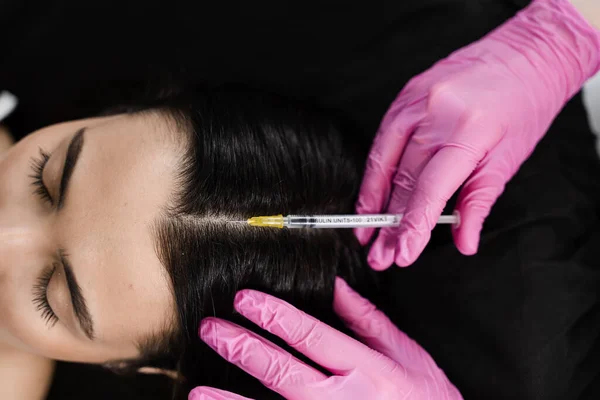 Cosmetologist is making mesotherapy injections in hair of girl top view. Mesotherapy treatment nourish the scalp and boost hair thickness and growth, helping to prevent hair loss