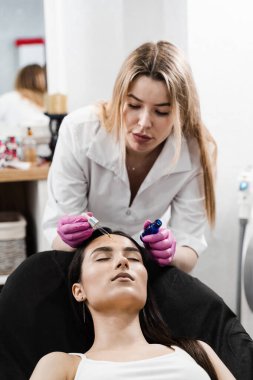 Dermatolog modelin yüzüne nemlendirici serum uyguluyor. Kozmetik uzmanı hasta kızın yüzüne pipetten hyaluronik asit ya da serum uyguluyor.