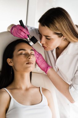 Cilt kanserini ve melanomayı önlemek için dermatoskopili deri lezyonları ve benlerin dermatoskopisi. Dermatolog dermatoskop kullanan kızın benlerini ve doğum lekelerini inceliyor.