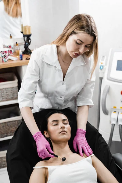 Process of face massage with black stone roller. Cosmetologist using stone roller for face massage for girl patient. Facial massage with cosmetics roller in cosmetology clinic