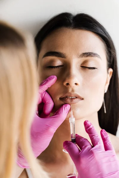 Lips augmentation injections for attractive girl. Cosmetologist injecting hyaluronic acid in lips for augmentation in medical clinic. Cosmetic rejuvenating facial treatment