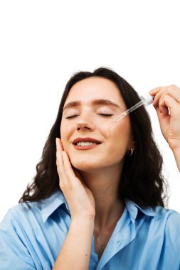 Genç bir kadın cilt yüzüne nemlendirici serum sürüyor. Elinde hyaluronik asit ya da serum pipeti olan kız.