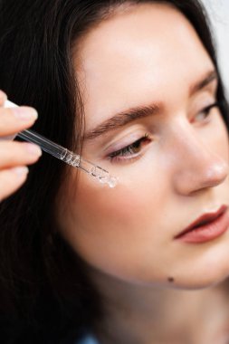 Elinde hyaluronik asit ya da serum pipeti olan bir kız. Genç bir kadın cildine nemlendirici serum sürüyor.