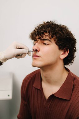 ENT doctor checking nose of man patient with rhinoscope. Rhinoscopy medical examination at a private ENT clinic before rhinoplasty or septoplasty surgery clipart